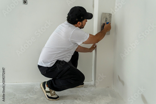 Builder applying smooth finishing layer on interior wall column using trowel in unfinished residential property under renovation and construction