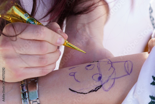 A person is drawing a cartoon character on another person's arm using a gold pen