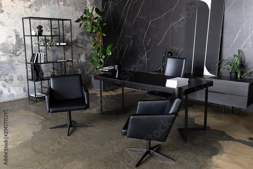 Modern luxury executive office interior design with dark marble wall, indoor plants, black wooden desk and leather chairs, premium black furniture, and minimalist decor.  