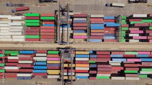 Aerial top-down view showing a gantry crane organizing colorful cargo containers at a busy port terminal, illustrating the complexity of global logistics and international shipping