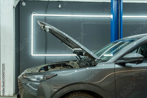 Gray sport utility vehicle parked indoors with the hood raised inside a modern automotive workshop, suggesting maintenance, inspection, or mechanical repair