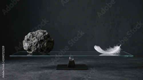 Rock and feather balance on glass scale in moody studio with dark background