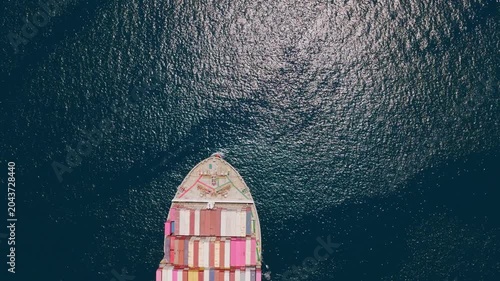 Impressive top-down aerial shot following a large container cargo ship as it sails across the vast open ocean, showcasing the scale of modern global trade and maritime shipping logistics
