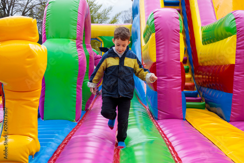 Принти на полотні A young boy running on a colorful bouncy castle at an outdoor amusement park, en