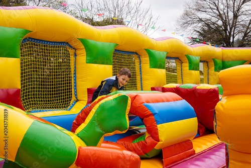 Tableau sur toile A smiling boy climbs over a colorful inflatable obstacle inside a bouncy castle,