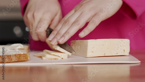 The housewife cuts the cheese with a knife in order to add it to the sandwich filling.