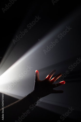 The fingers of a hand cross a beam of white light that forms angles against a black background. Lighting effect. White light on a black background. Spotlight.