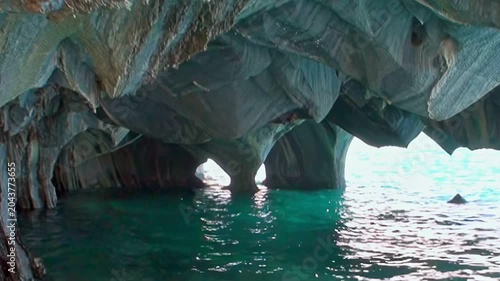 Witness sunlight dancing on pristine blue waters, flowing beneath ancient, sculpted marble arches within the glorious Marble Caves of Patagonia. A serene daytime exploration.