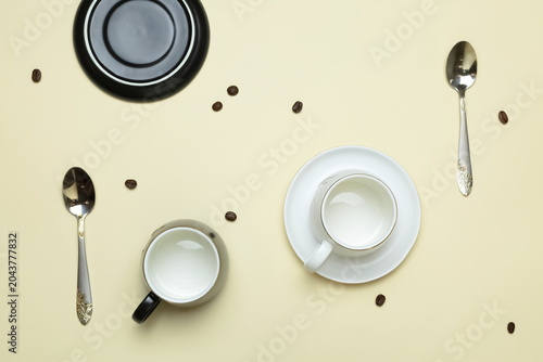 coffee cups, saucers, and spoons with scattered coffee beans on a beige background. Top view.