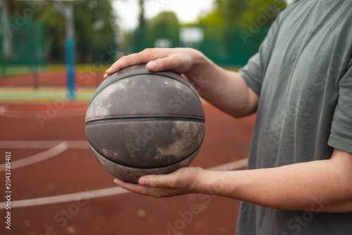 Cropped view of a young male basketball player holding a ball in front of him on an outdoor court
