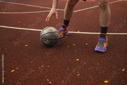 Cropped view of a basketball player dribbling a ball on an outdoor court surface during training