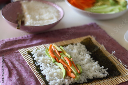 Making vegan sushi rolls at home. Bamboo mat, nori sheets, rice, cut vegetables and soy sauce on the table. Selective focus.