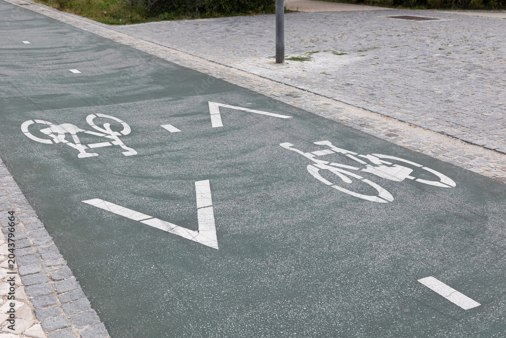 Obraz premium Urban bicycle lane with painted bike symbols and directional arrows on asphalt pavement. Dedicated cycling infrastructure in a modern city promoting sustainable transport, eco-friendly mobility
