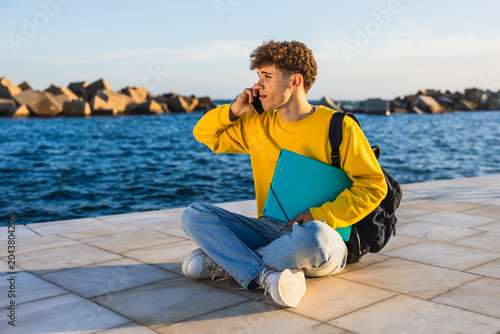Young student talking on smartphone while sitting by the sea