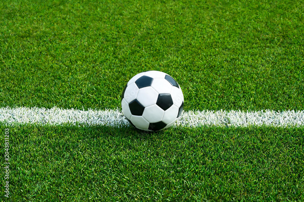 Fototapeta premium Balón de fútbol clásico sobre césped verde impecable colocado exactamente en la línea blanca del campo de juego. Concepto de saque inicial, reglas del juego, comienzo del partido y torneo.