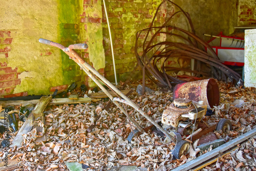 Schilderij op canvas Rusty old lawn mower abandoned in a cluttered shed with dry leaves and debris