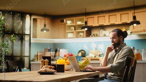 Quadro em tela Uncertain freelancer being confused about ambiguous tasks at home, remote work on laptop in the kitchen, Disoriented disorganized man unsure about telecommuting job, frowning
