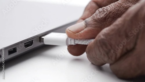 Closeup of a persons hand plugging a white usb cable into a laptop port