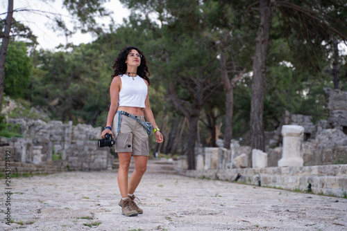 Young female photographer walking with camera in ancient ruins or nature park.