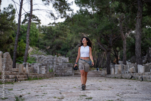Young female photographer walking with camera in ancient ruins or nature park