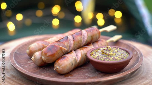 Sizzling Bacon-Wrapped Sausages with Grainy Mustard on Rustic Plate, Festive Outdoor Dining Ambiance.