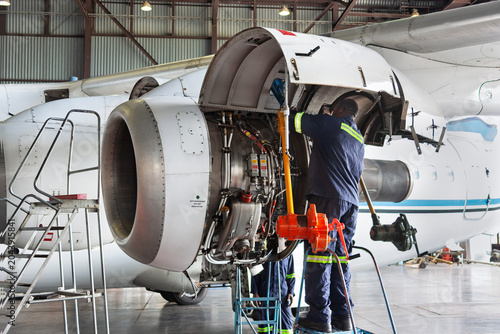 Aircraft mechanics performing maintenance on turboprop jet engine in hangar