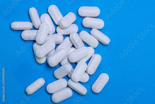 White medicine pill capsules scattered on blue background.