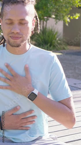 Vertical video: Breathing man in sun taking slow chest-belly breaths on deck, opening eyes smiling