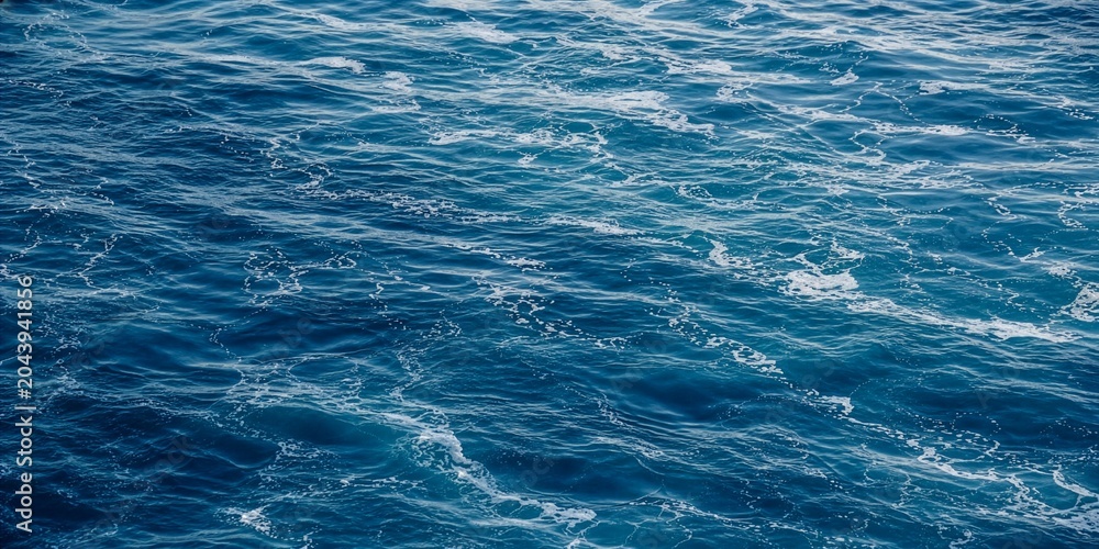 Obraz premium Deep Blue Ocean Water Surface Texture with Gentle Ripples, Flowing Waves, and White Sea Foam Creating a Calming Aquatic Background