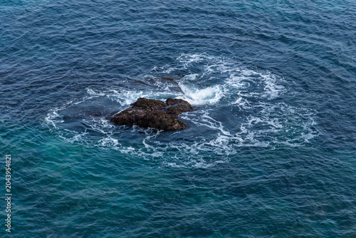Ocean waves swirling around a dark solitary reef stone