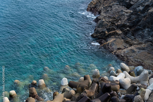 Concrete tetrapods and rocky cliff along clear emerald coast