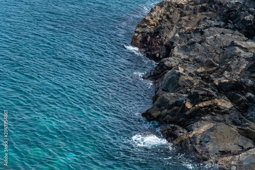 Top view of ocean waves crashing against dark rocky cliff
