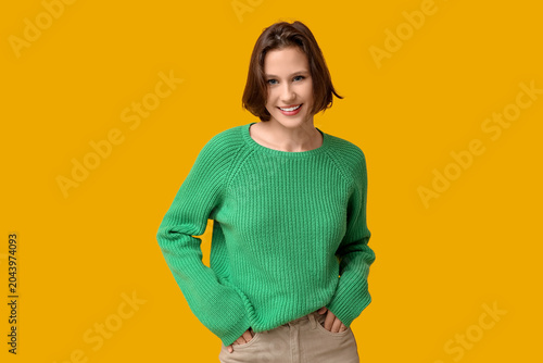 Beautiful young woman in stylish green sweater on yellow background