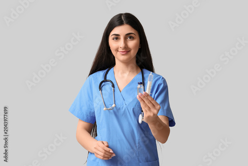 Beautiful young female doctor with stethoscope, syringe and ampule on white b...