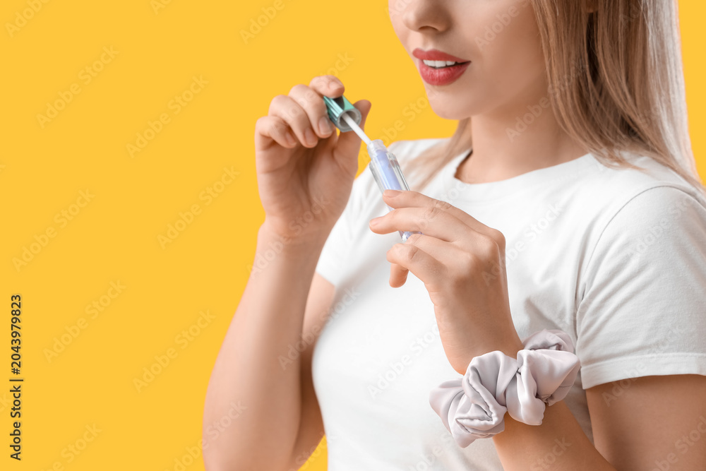 Fototapeta premium Young blonde woman with scrunchy and lip gloss on yellow background, closeup