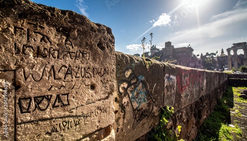 Rough textured ancient stone wall with Latin etchings and graffiti under a sunny blue sky