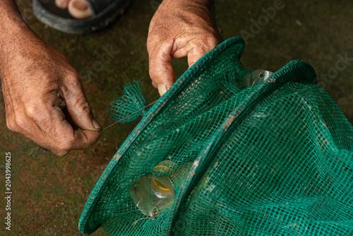 Bilde på lerret Close up of an elderly fisherman hands weaving or repairing a green plastic mesh fish trap