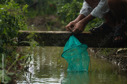 Photos A Vietnamese farmer setting a green plastic mesh fish trap into a rural canal water