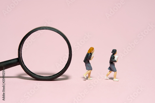 Miniature people toy figure photography. Two girl pupil students running in front of magnifier glass. Isolated on pink background