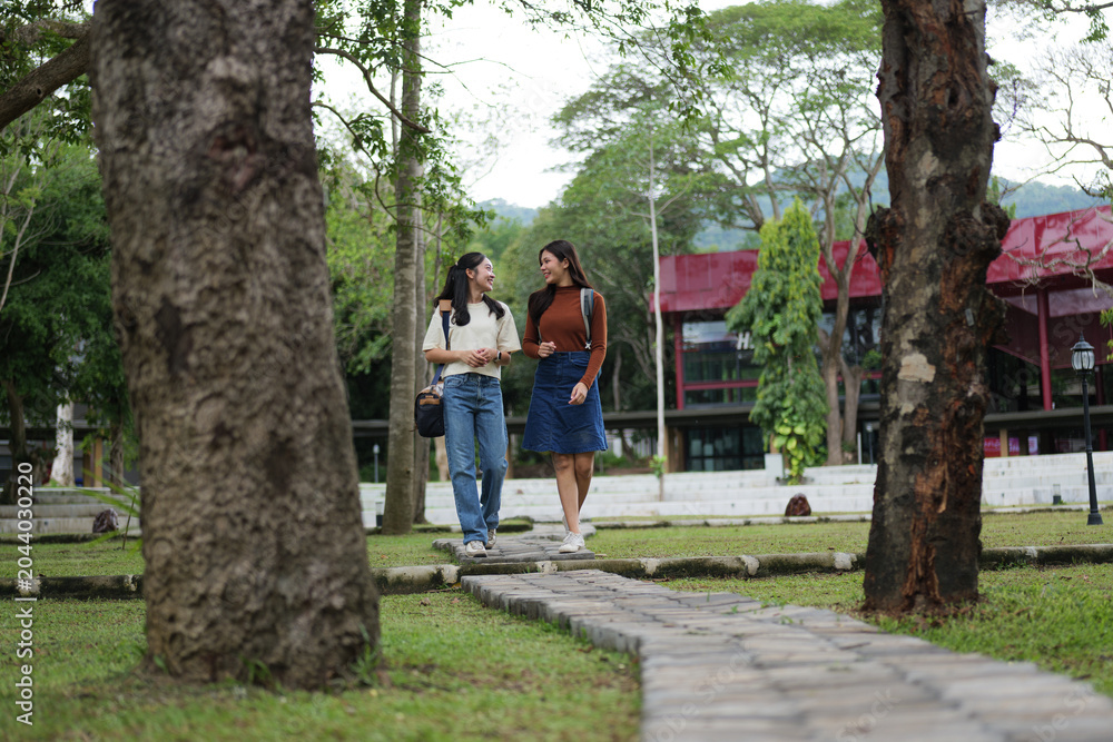 Obraz premium Young women students walking talking on university campus path