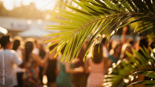 Close up of tropical palm leaves with blurred background of people enjoying a sunny outdoor gathering