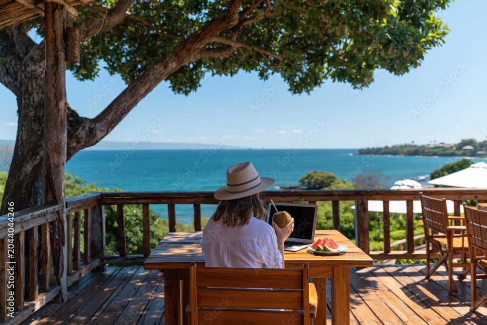 Obraz premium Remote work woman with laptop on sunny terrace overlooking tropical ocean view