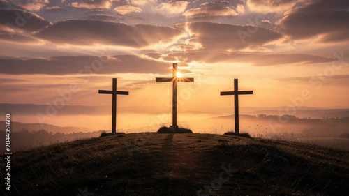Three wooden crosses on hill at sunrise with dramatic sky and misty landscape in the background