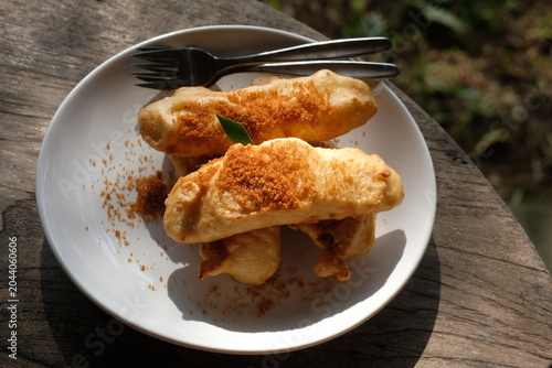 banana fritters with sprinkle palm sugar on a white ceramic plate. Indonesian food. pisang goreng.