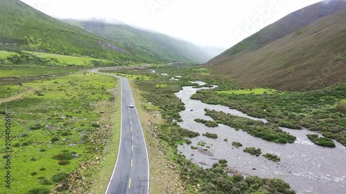 Aerial view of winding road and river in misty green mountain valley