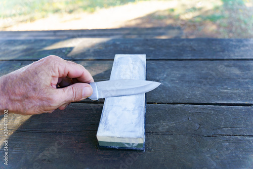 Person's hand honing a knife blade on a long whetstone, performing blade maintenance for precision and sharpness