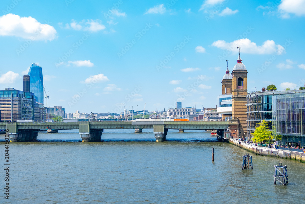 Obraz premium London Bridge spans River Thames modern glass skyscrapers historic brick towers blue sky cityscape, British capital urban waterfront architecture, England UK landmark skyline, United Kingdom tourism