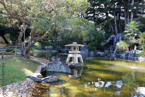 A stone lantern standing in a tranquil pond flanked by rocks and a gentle tiered waterfall at the Rockhampton Botanic Gardens in Queensland, Australia