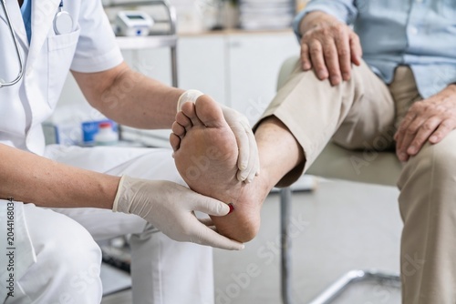 Woman doctor examining elderly man foot ulcer. Treating diabetic wound on heel. Medical healthcare concept for geriatric care