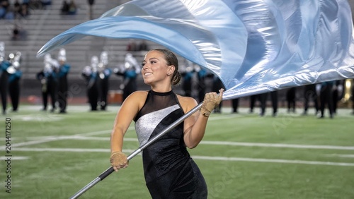 Young woman performing with a flowing blue flag on a sports field, part of a marching band